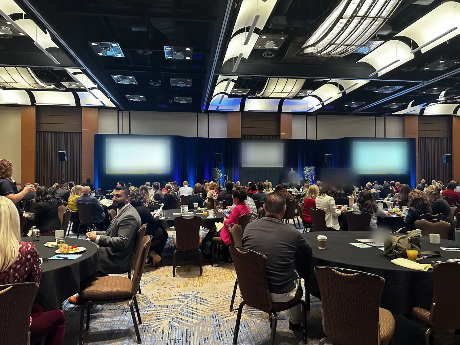 A packed ballroom general session at an association conference, speakers on stage