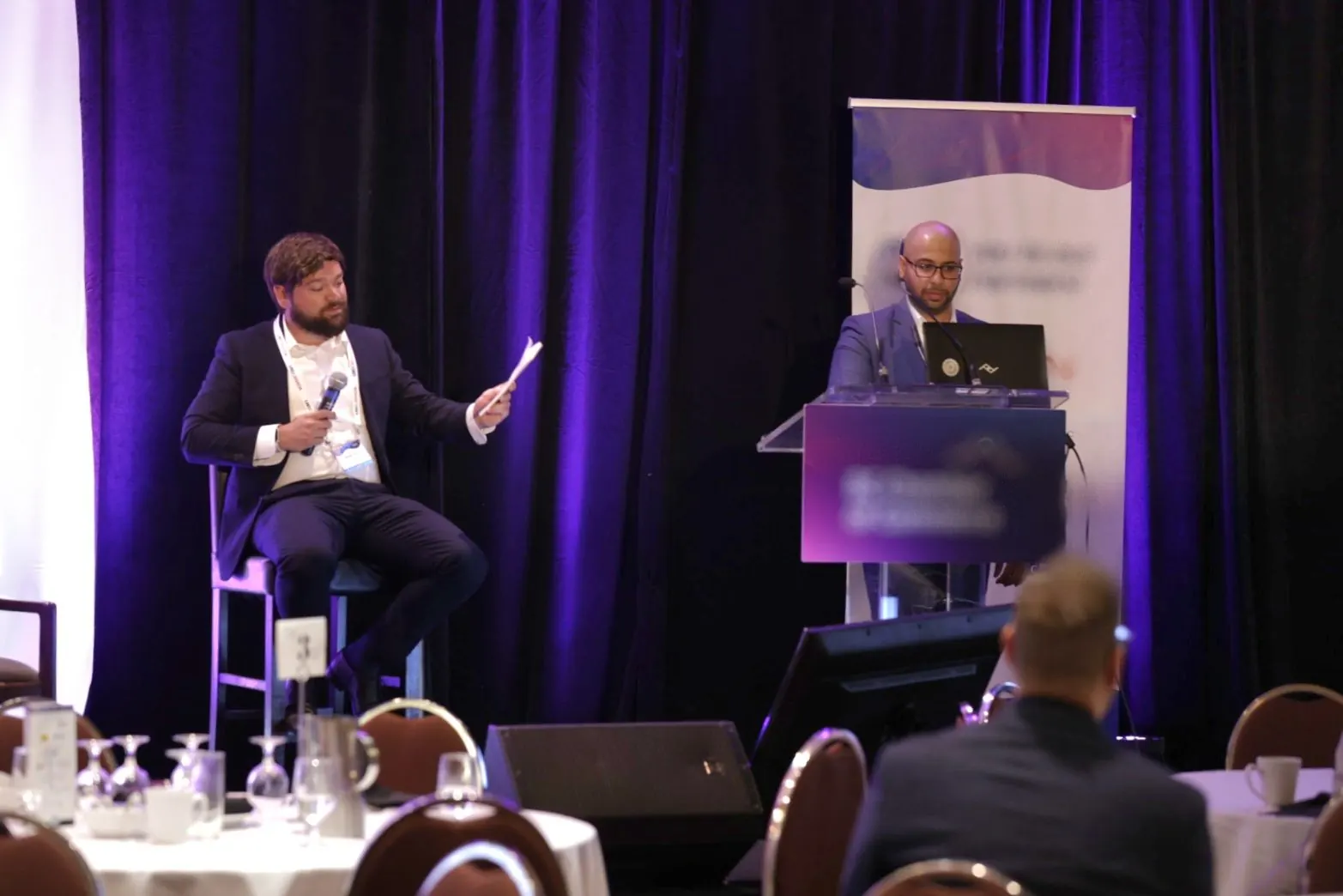 Panelists speaking on stage in front of a round-table audience